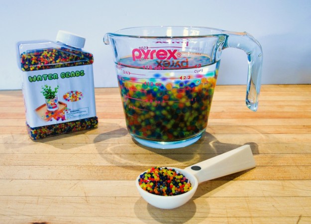 A glass measureing cup is filled half with expanding beads and half with water.