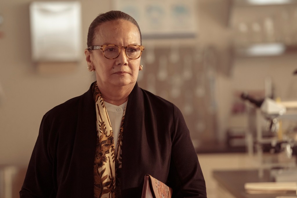 A woman in a small laboratory looks grimly toward the middle distance.