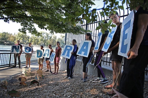 A group of people each holding a sign with a letter on it, the line of signs spells "NO DAM RAISE"