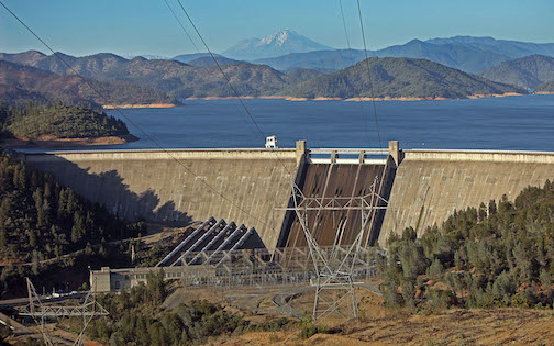 A dam with water behind it, and in the far background are mountains.