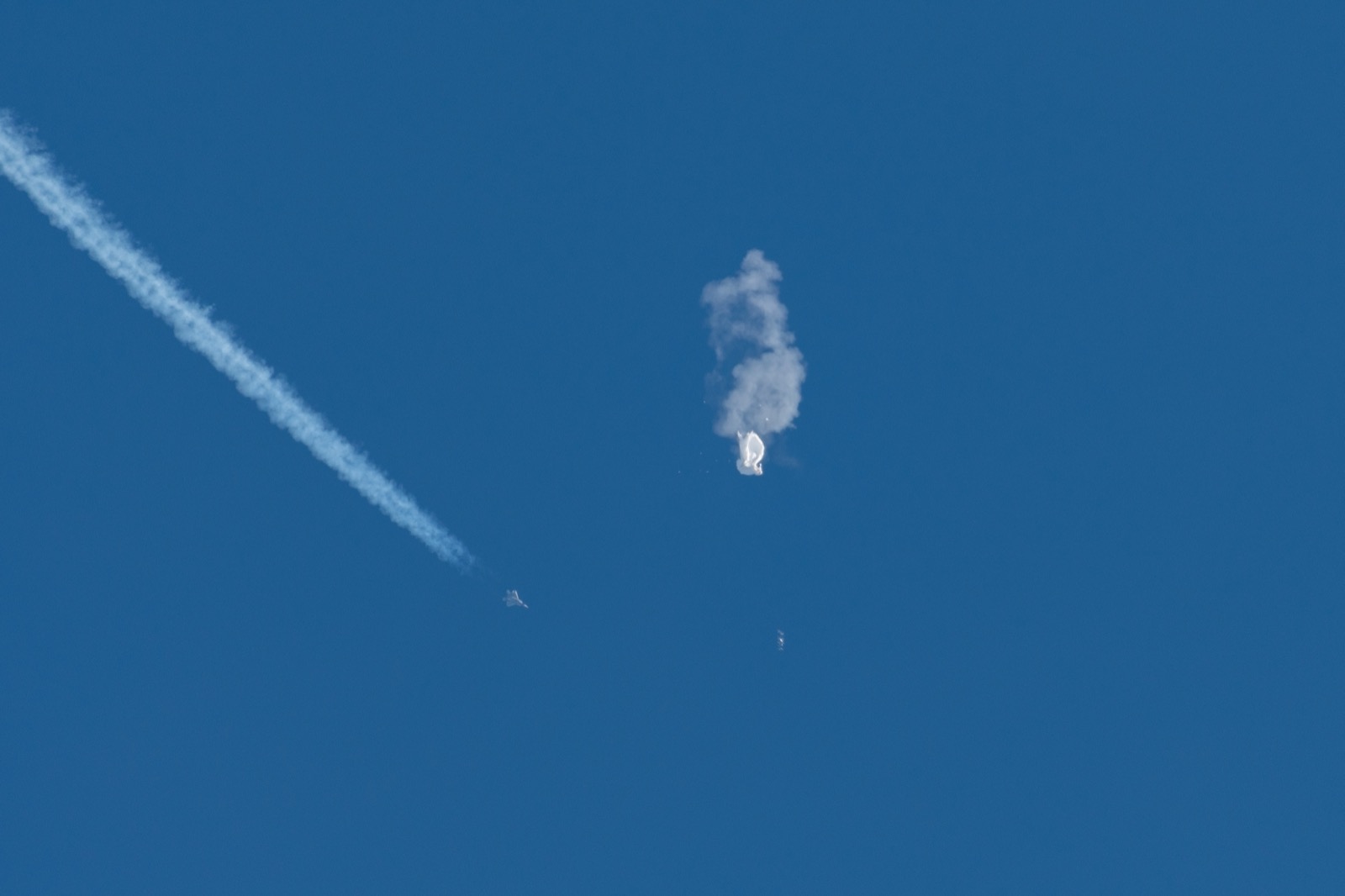 a zoomed in image of a deflated white balloon in the sky, and a fighter jet zooms by off to its left