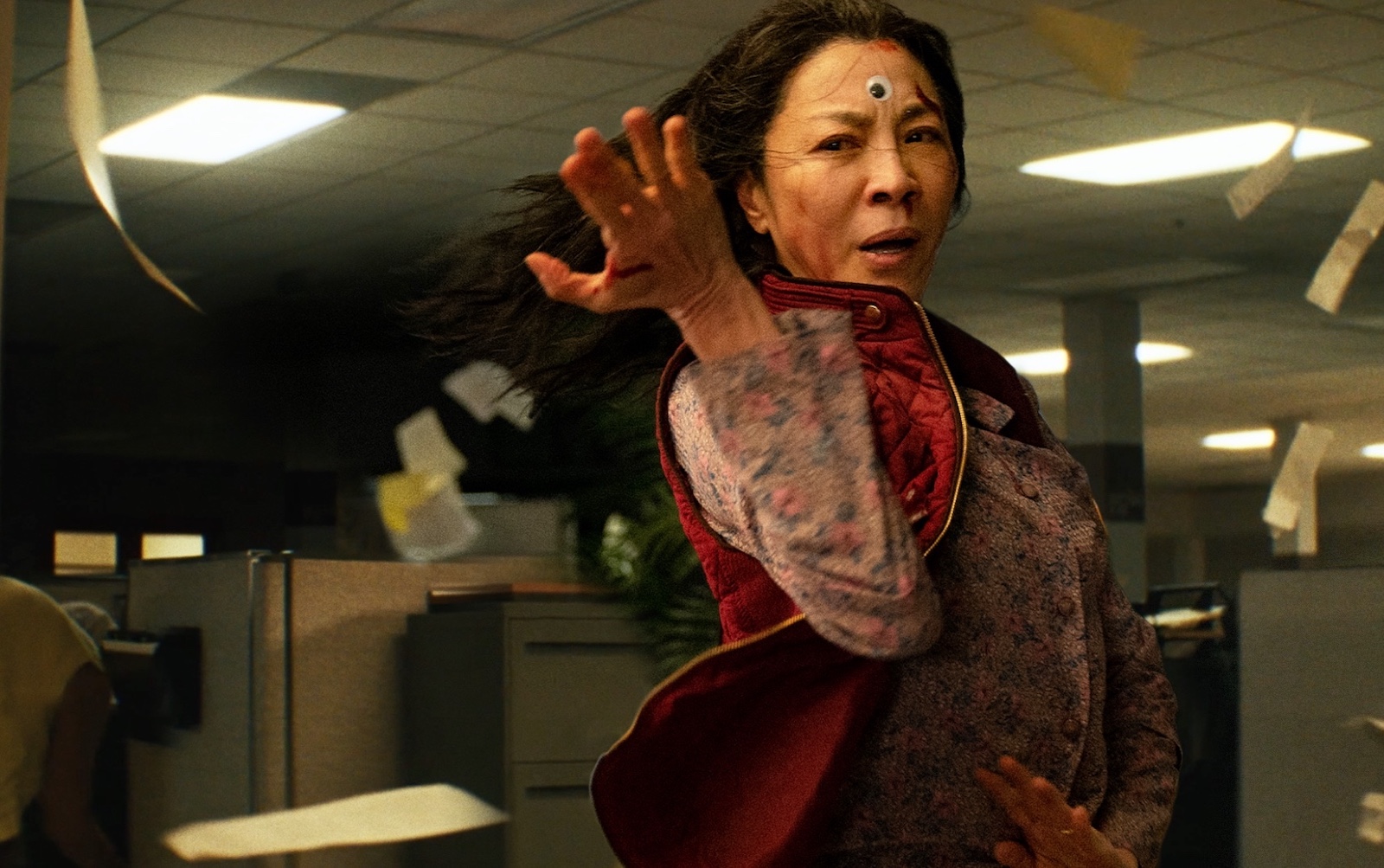 a fierce malaysian woman, actress michelle yeoh, portrays a middle-aged chinese immigrant and laundromat owner. she adorns a goofy google-y eye on her forehead and stands in a martial arts position, ready to fight