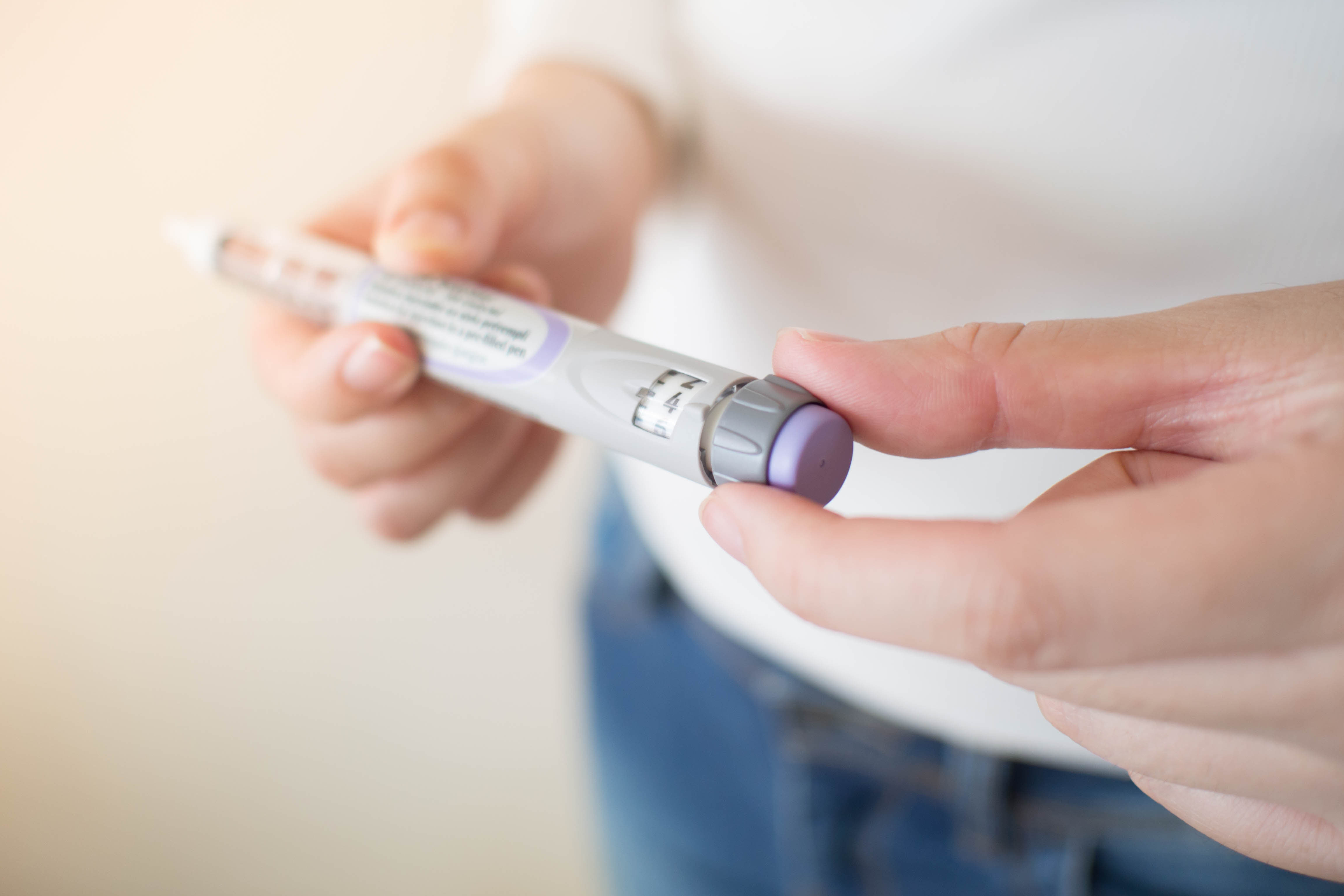 a white pair of hands holding a vial of insulin