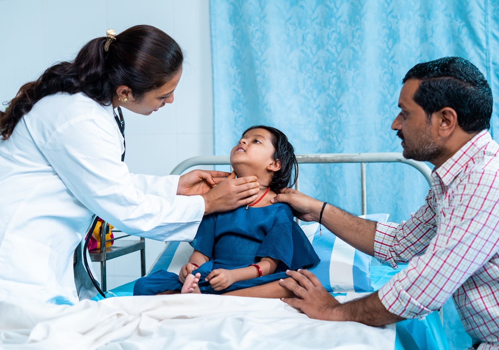 a doctor examines the throat of a young child who is with their father. the doctor is gently touching the child's throat near their jaw and ears, where mumps typically causes swelling