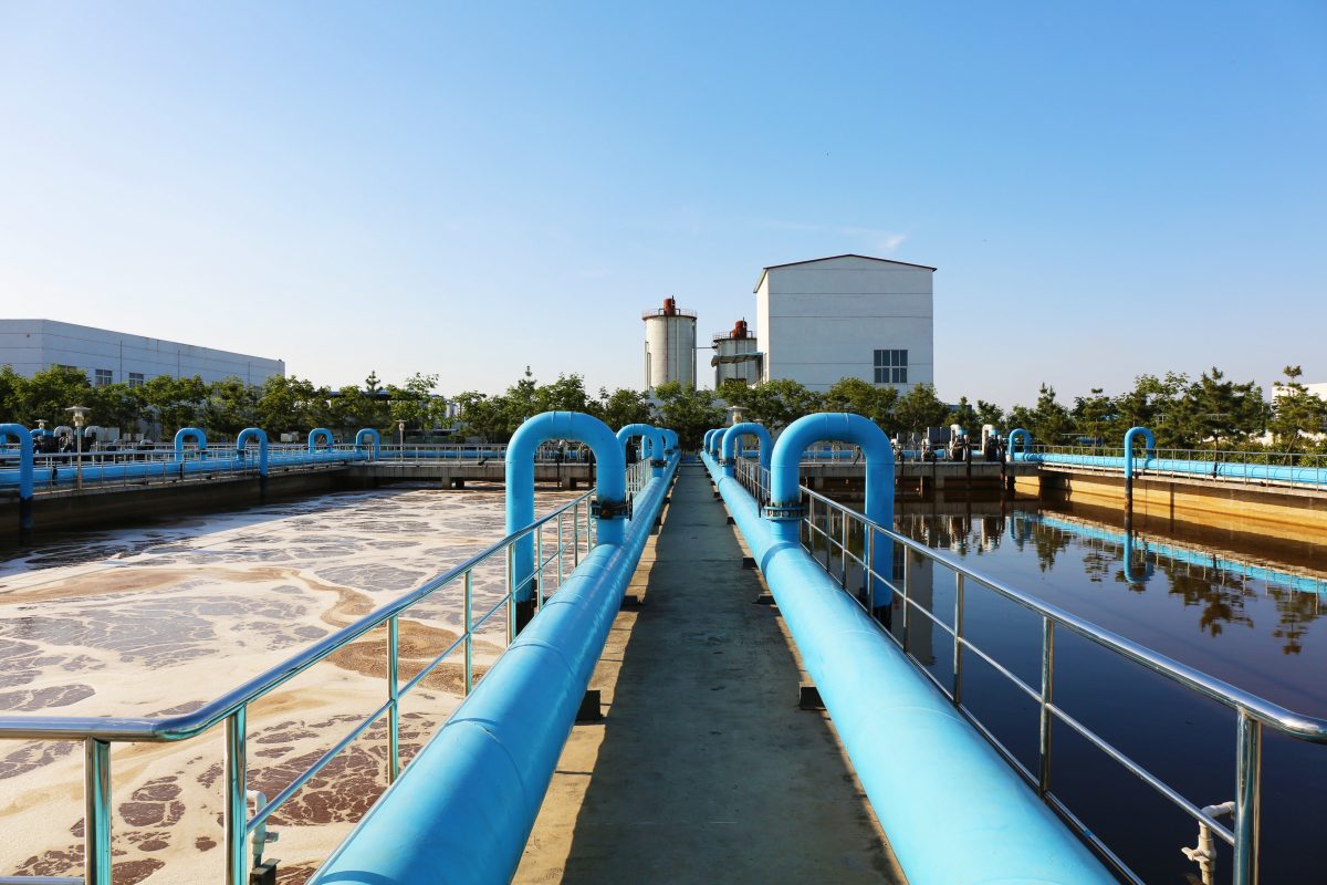 A view between two wastewater treatment tanks the size of swimming pools, on the left one is churning and brown and on the right is a tank that is glassy and still. Both tanks are the size of swimming pools.