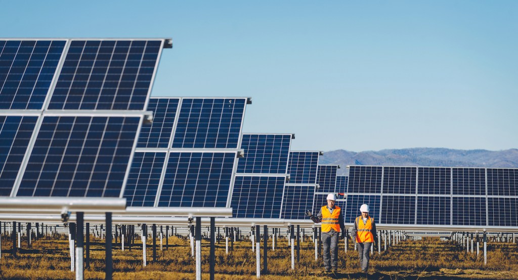 solar power station with two people in hard hats walking through many solar panels