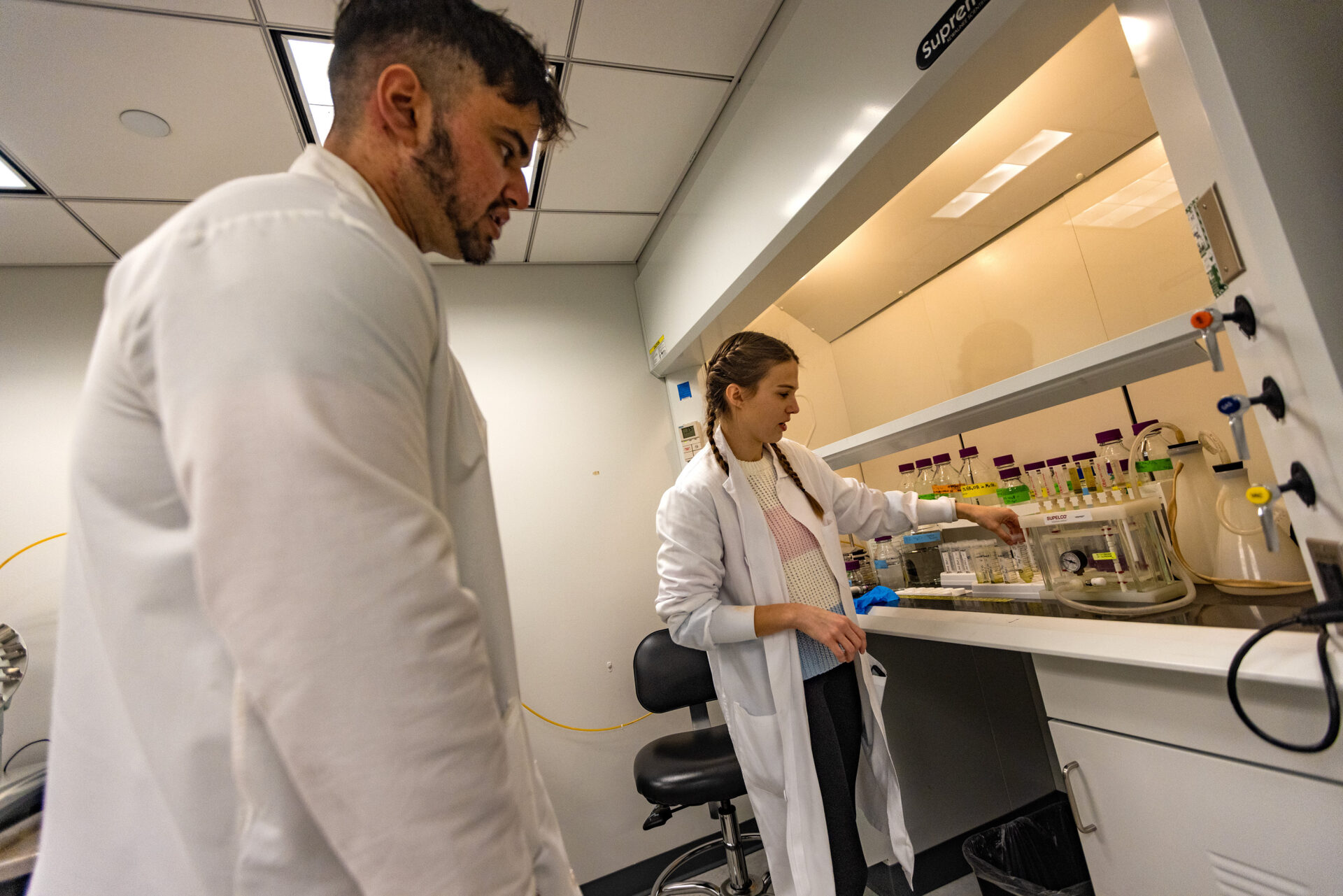 Two people work in a lab underneath a fume hood. 