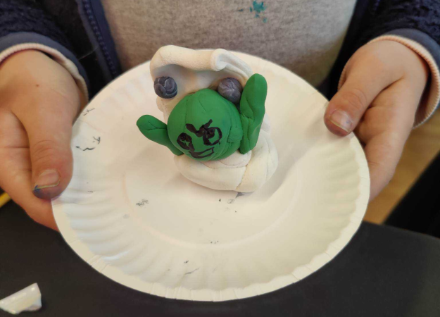 A green frog in a white toilet modeled out of clay.