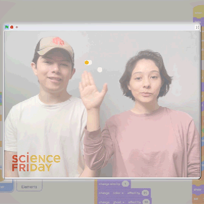 Two young people move their hands through the air to control the computer screen.
