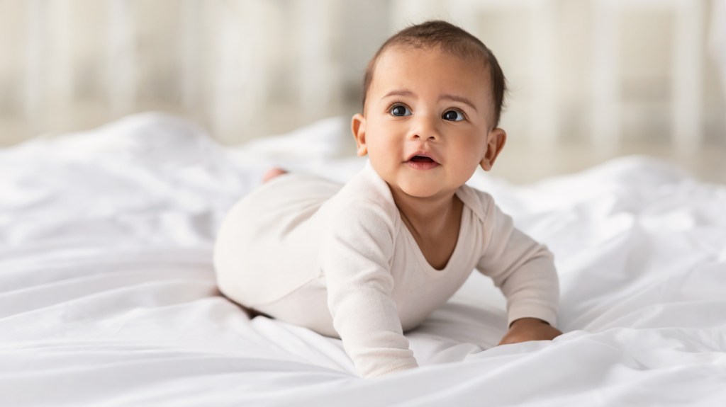 Childcare Concept. Portrait of cute baby wearing bodysuit lying on white beedsheets at home.