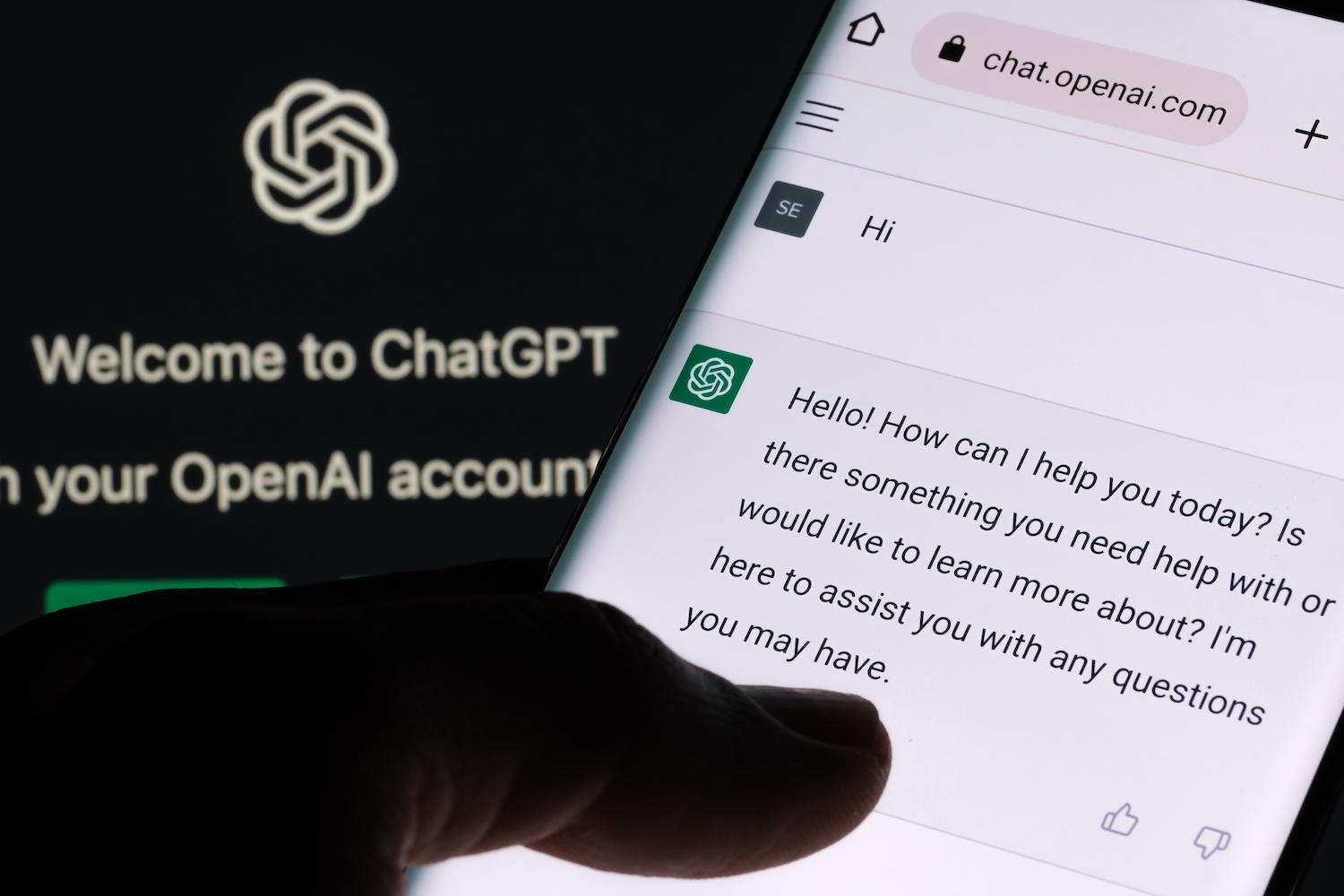 a person's thumb scrolls over a phone that has a chat bot open, which is chatgpt. in the background is chatgpt and open ai's logo, which is a hexagonal swirl