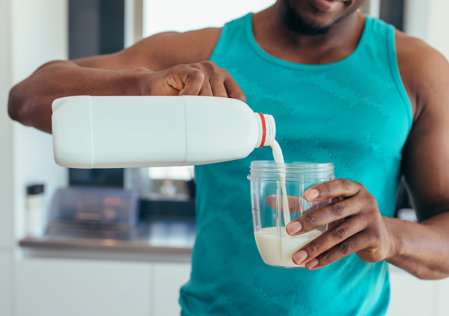 a black man in a blue tank pouring milk in a glass.