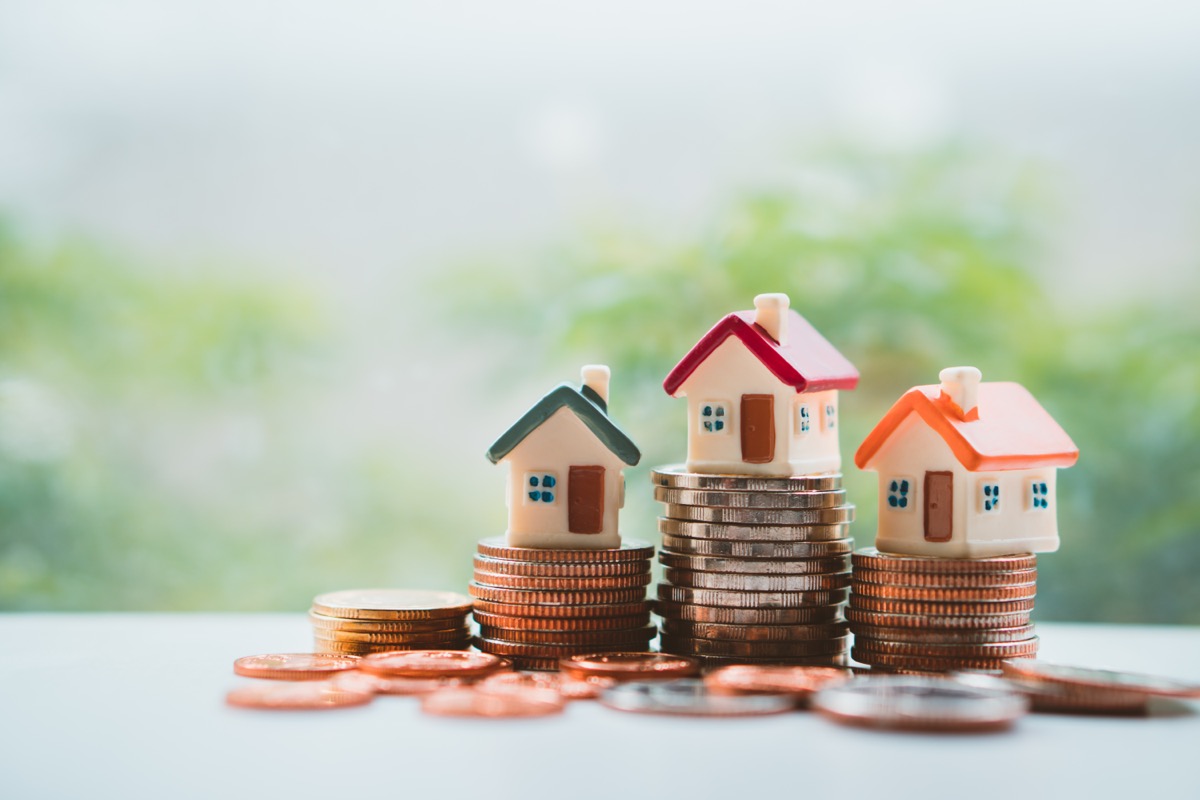 Colorful miniature houses sitting on stacks coins.