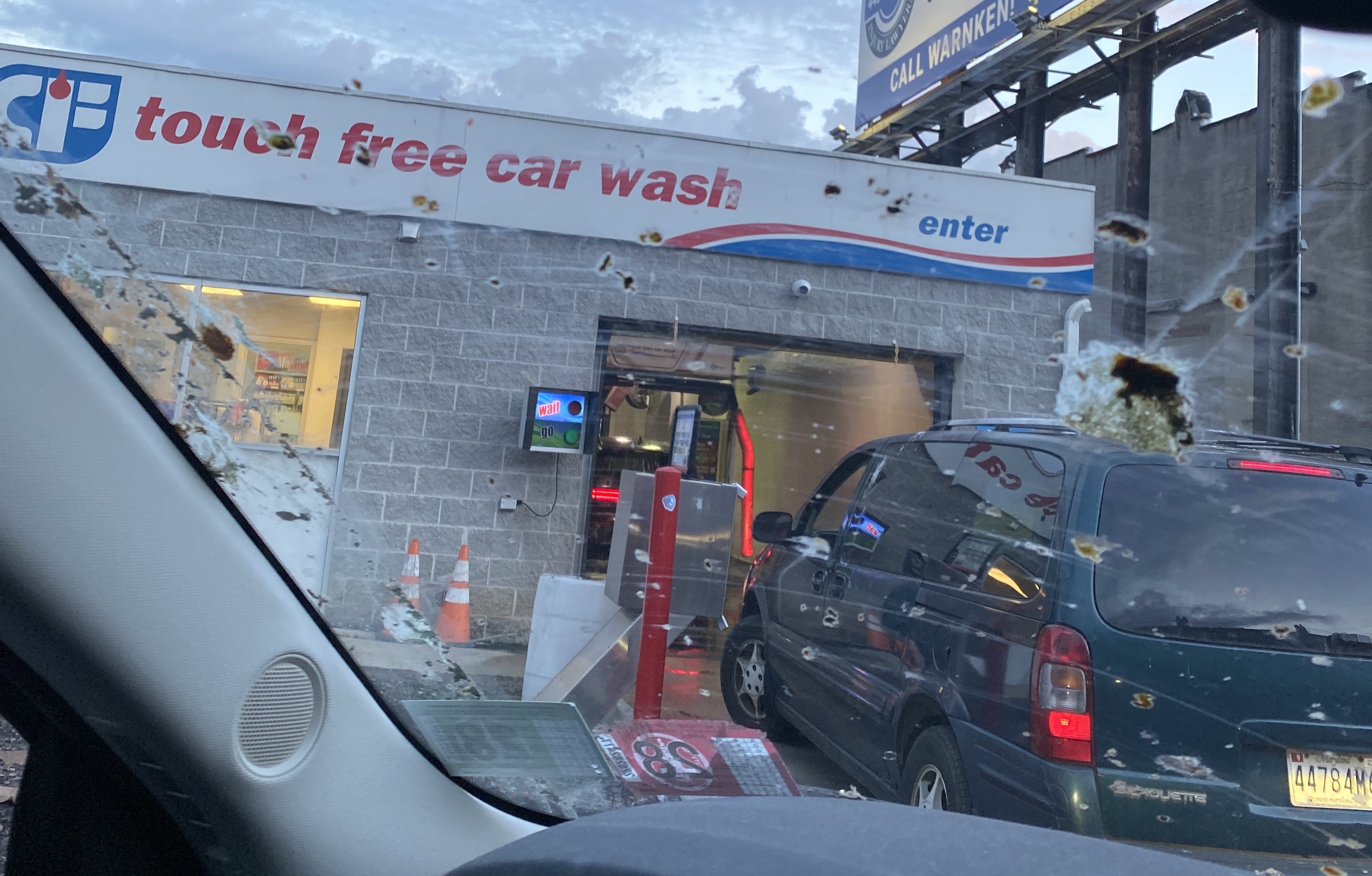 looking from the inside of a car, whose windshield is covered in bird poop, looking out onto a car wash