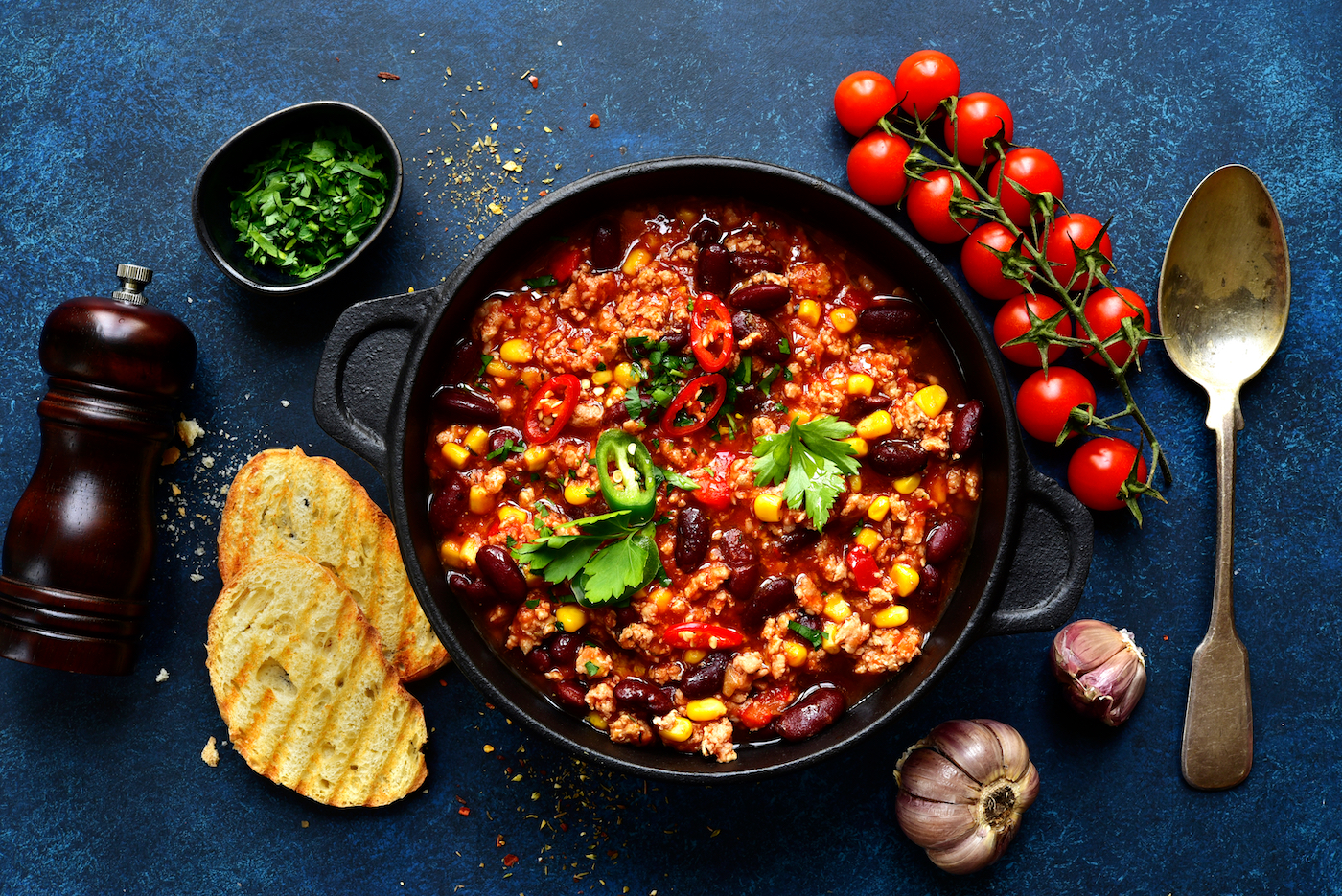 Chili con carne - traditional mexican minced meat and vegetables stew in tomato sauce in a cast iron pan on a dark blue slate, stone or concrete background. 