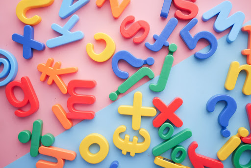 Colorful plastic letter magnets on a pink and blue background.
