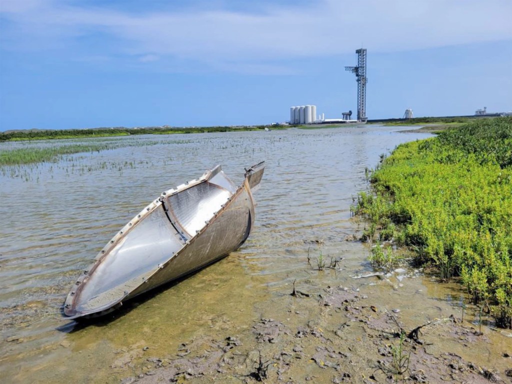 A piece of a rocket resting in a shallow pond, not far from the launch pad