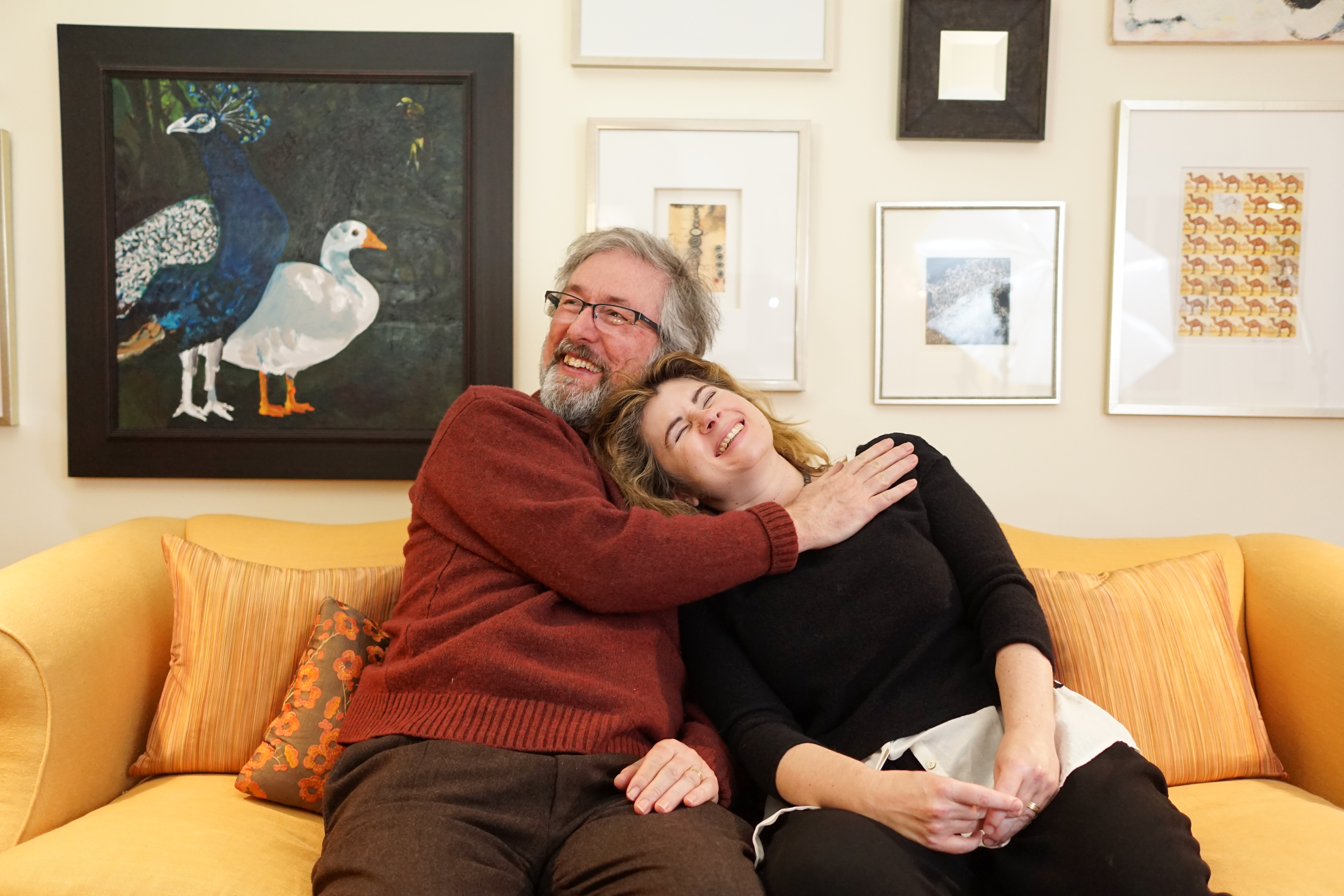 Two middle-aged people hugging and smiling on a yellow couch