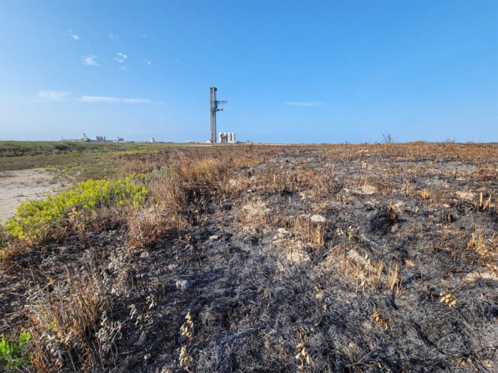 Burnt vegetation with a rocket launchpad in the background.