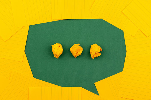 A speech bubble shape formed by the placement of gold-colored pieces of paper on a dark green background.