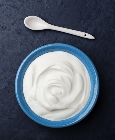 Greek yogurt in blue bowl on black table top view.