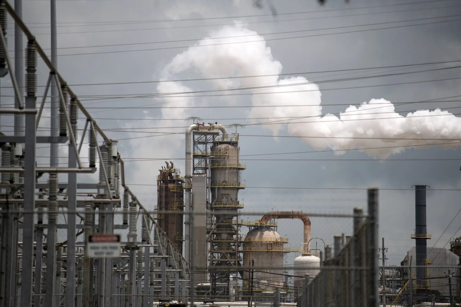 Large, towering industrial parts of an oil refinery loom in the sky. 