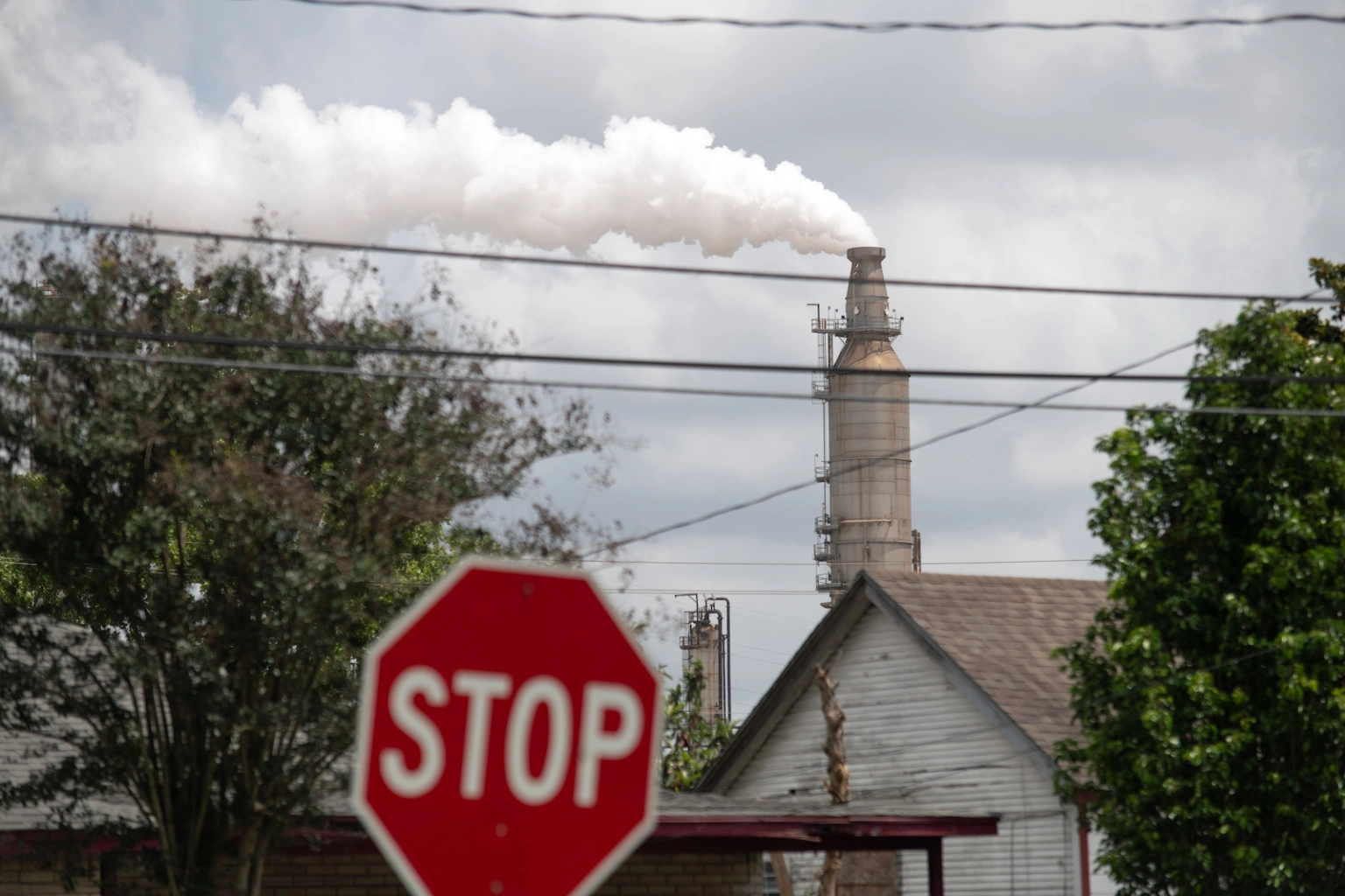 A smoke stack towers above a residential area emitting a cloud of pollution.