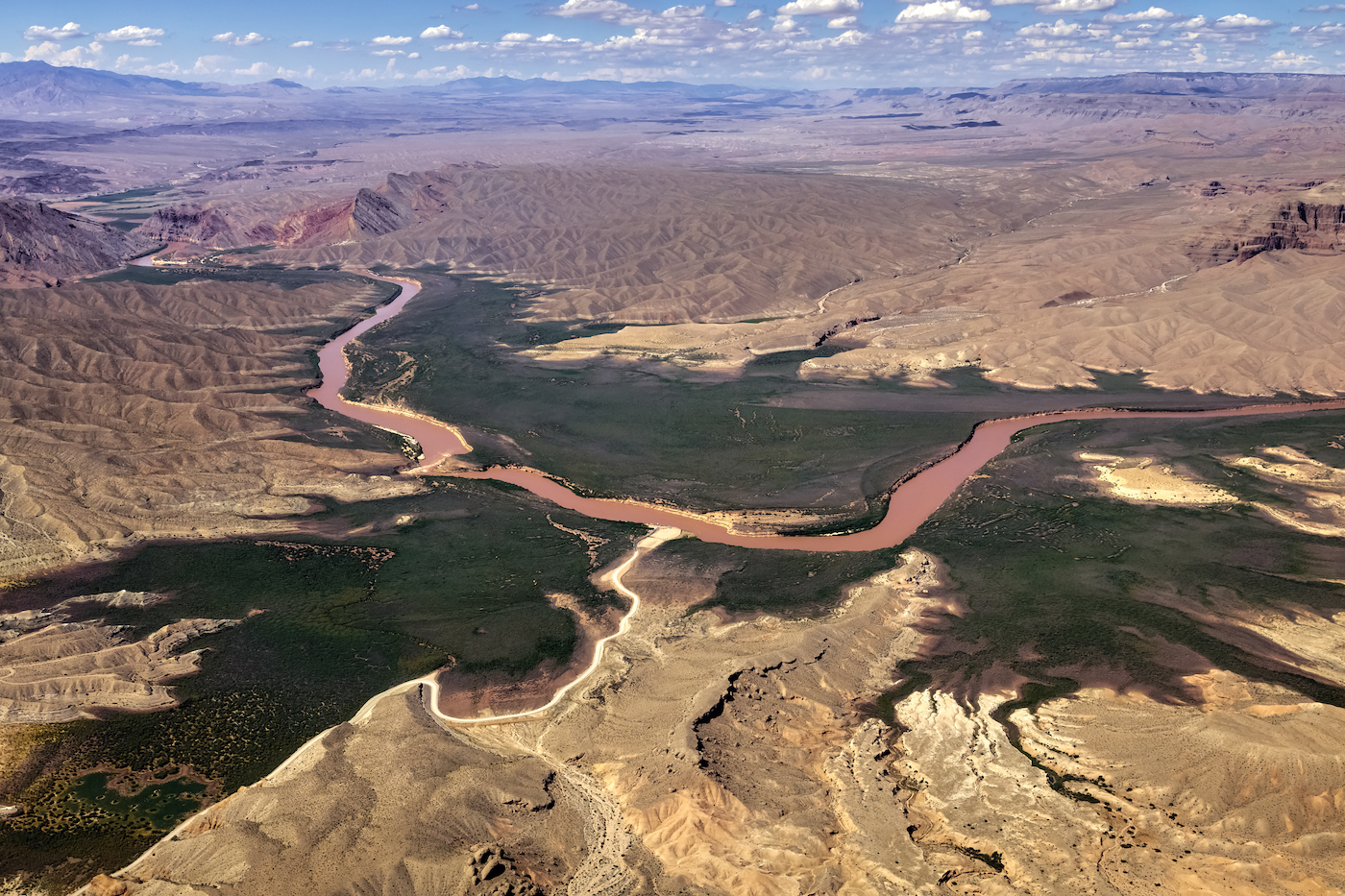 An aerial view of the twisting Colorado river, with green vegetation surrounding the banks and dry desert further away.