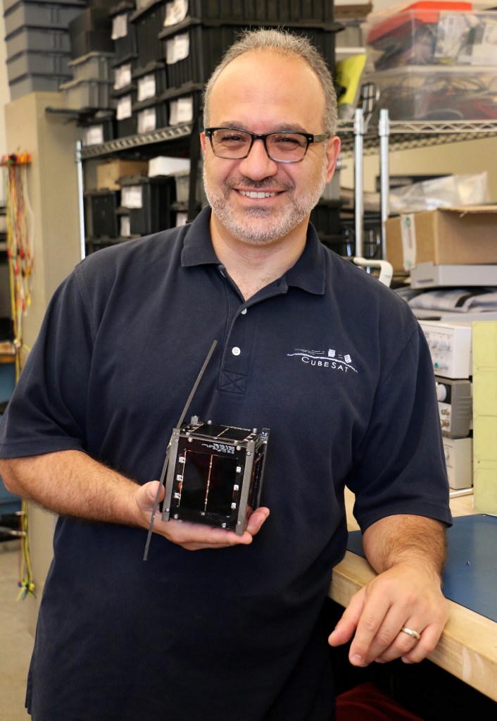 A man holding up a small cube about the size of a tissue box. It's black, and looks like it's made out of computer chips.