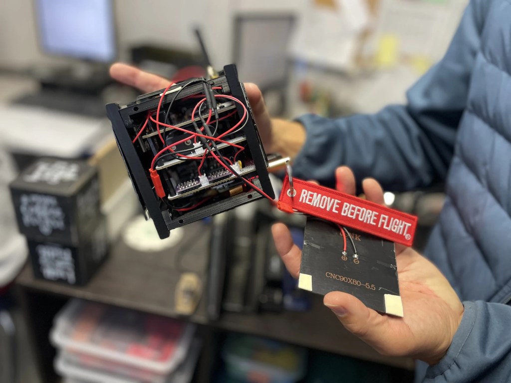 A pair of hands hold up a small piece of technology: two squares connected by some wires. 