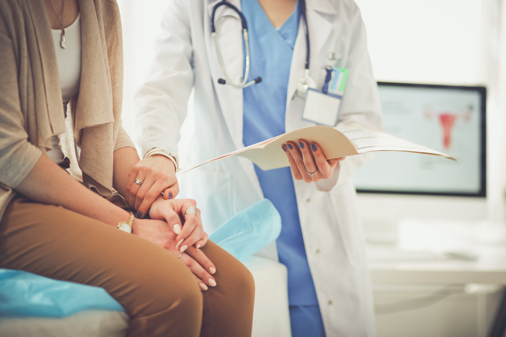 a female doctor places her hand on a female patient's arm who is sitting on a exam table