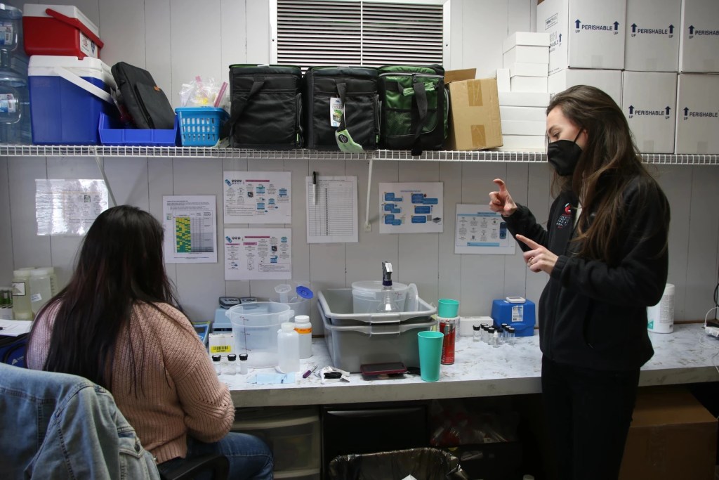 Two women sit in a lab holding test tubes