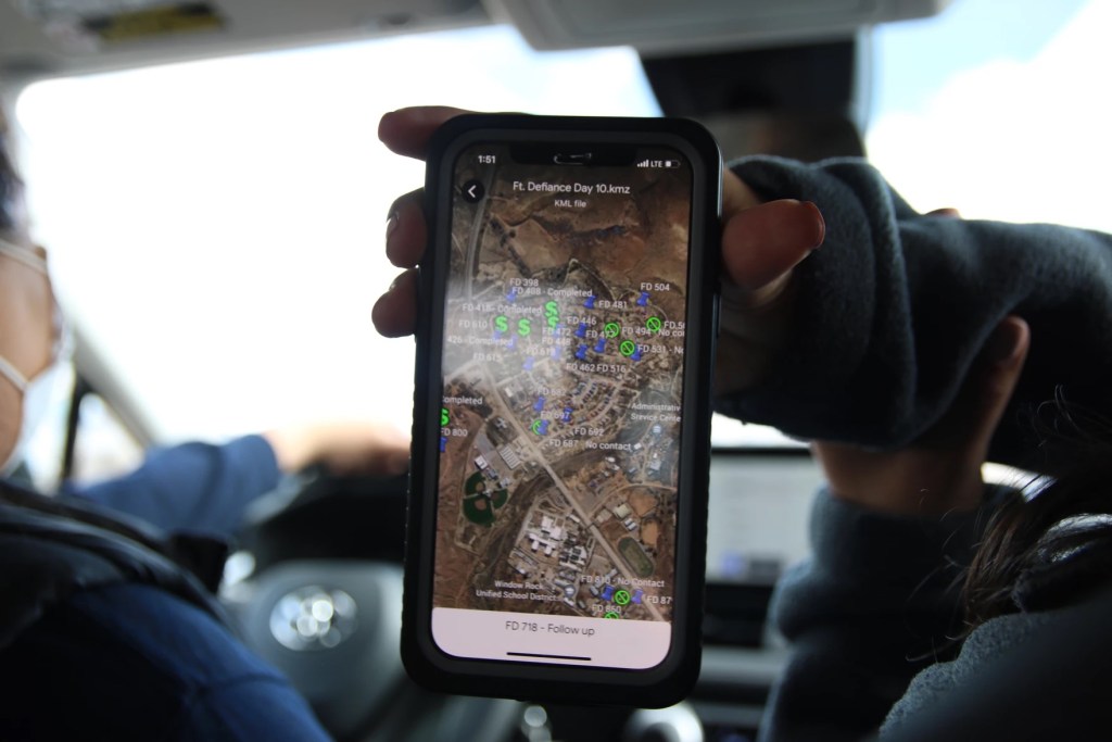 A hand holds up a phone GPS map in a car. 