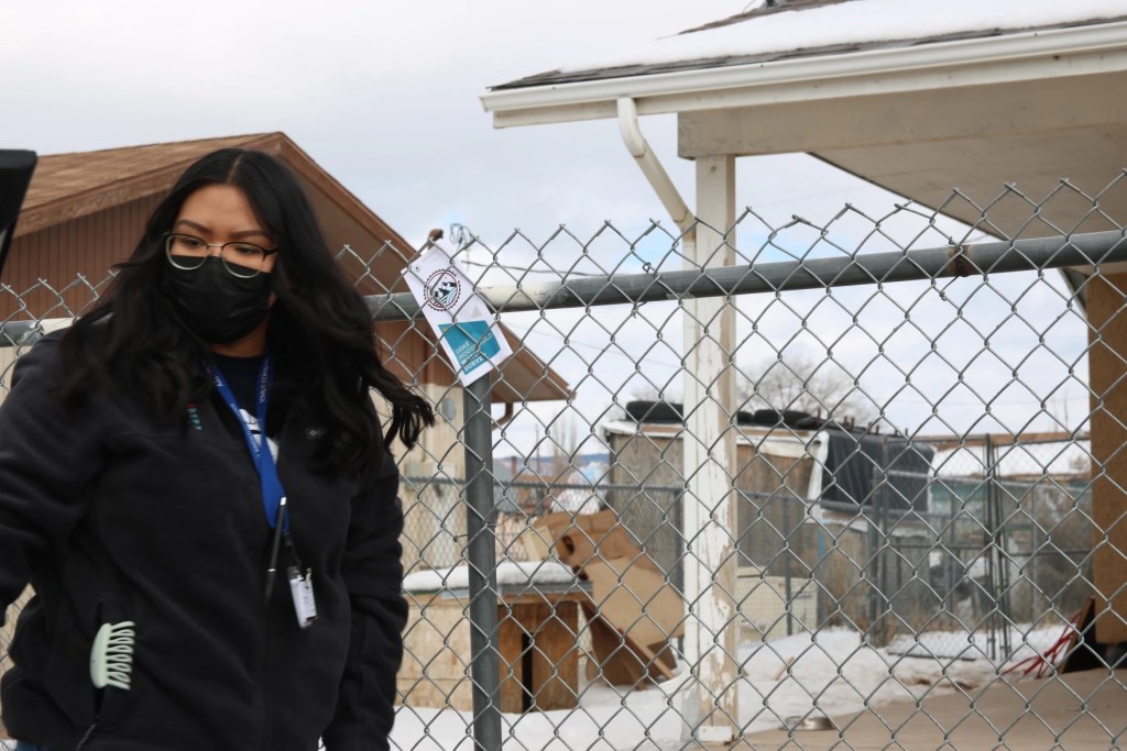 A woman wearing a face mask standing by a metal gate. 