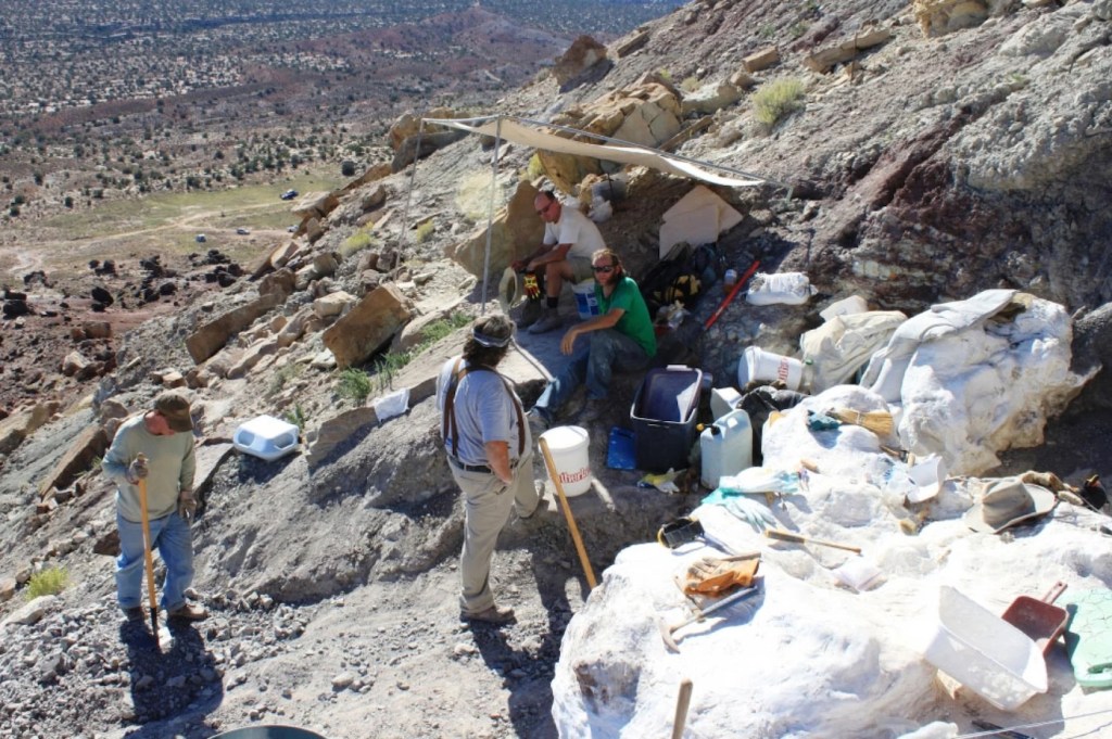 A group of people rest under a makeshift shelter along the side of a rocky mountain
