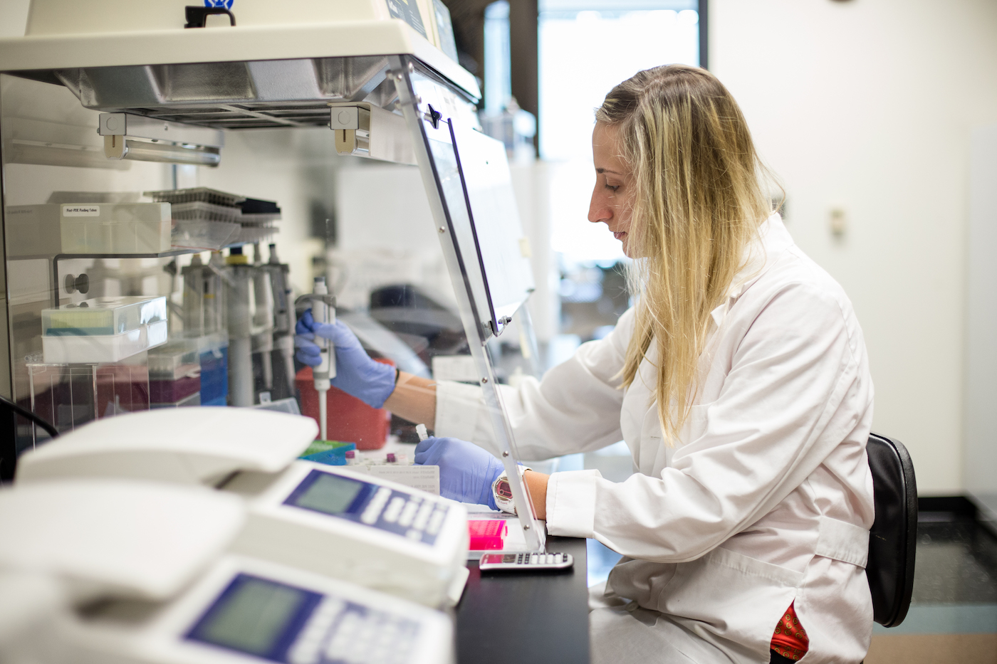 A woman pipetting something into tubes under a fume hood in a lab.