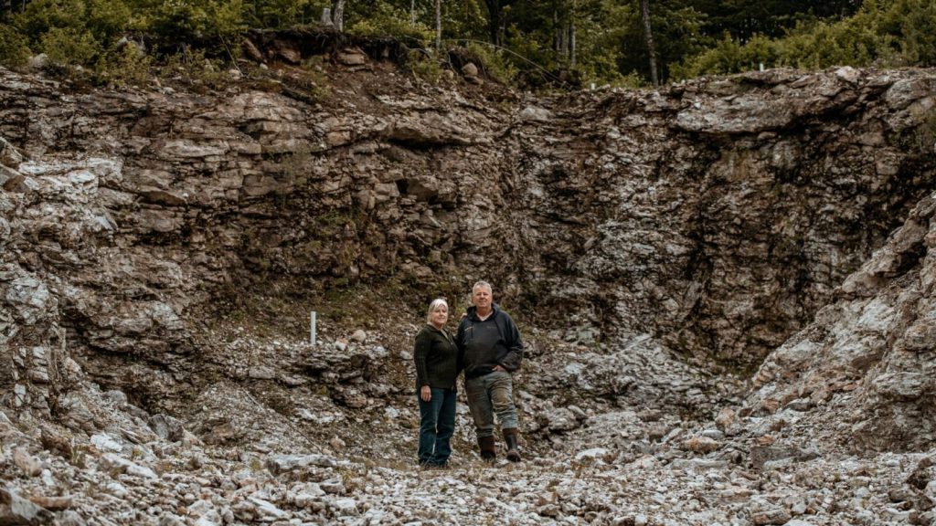 A man and woman dressed in hiking clothes and boots stand next to each other in the bottom of a large stony quarry.