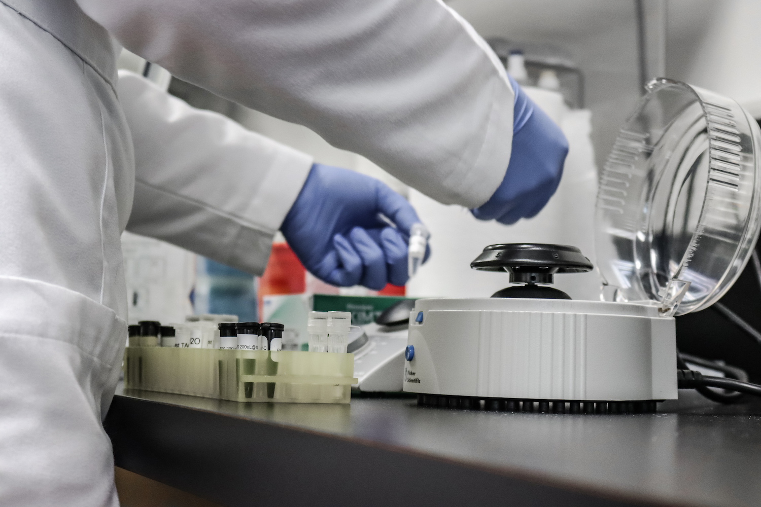 A scientist in gloves and a lab coat puts test tubes into a centrifuge.