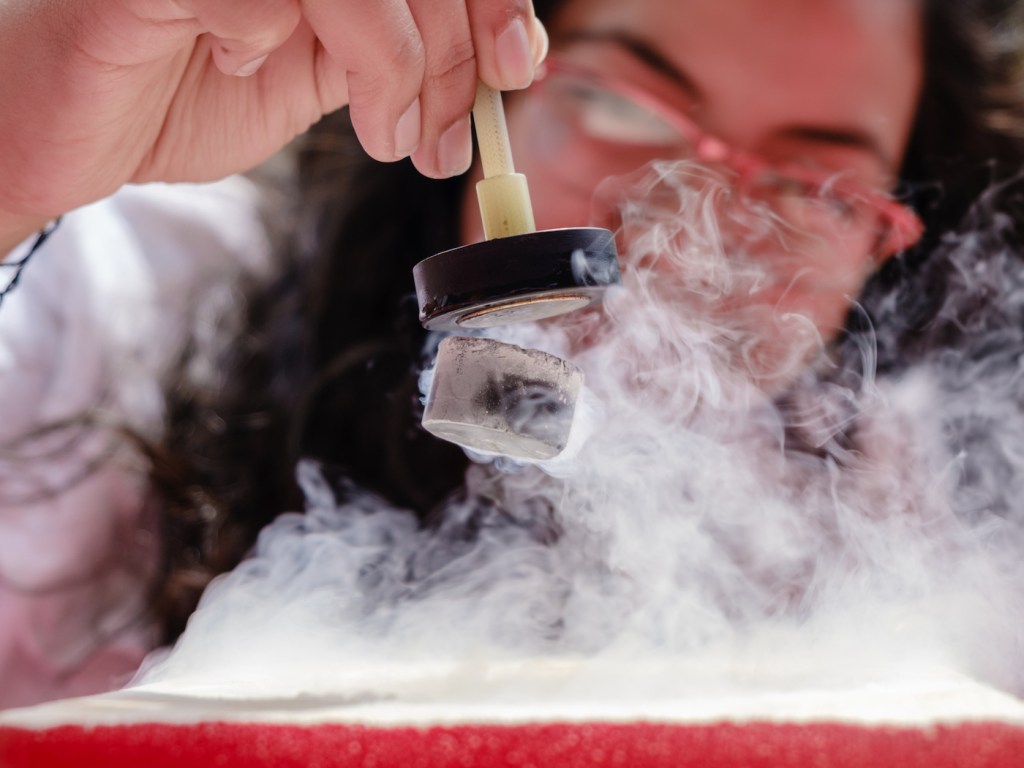 Female Student Demonstrates Quantum Magnetic Levitation and Suspension Effect. A splash of liquid nitrogen cools a ceramic superconductor forcing it to float in air below a magnet