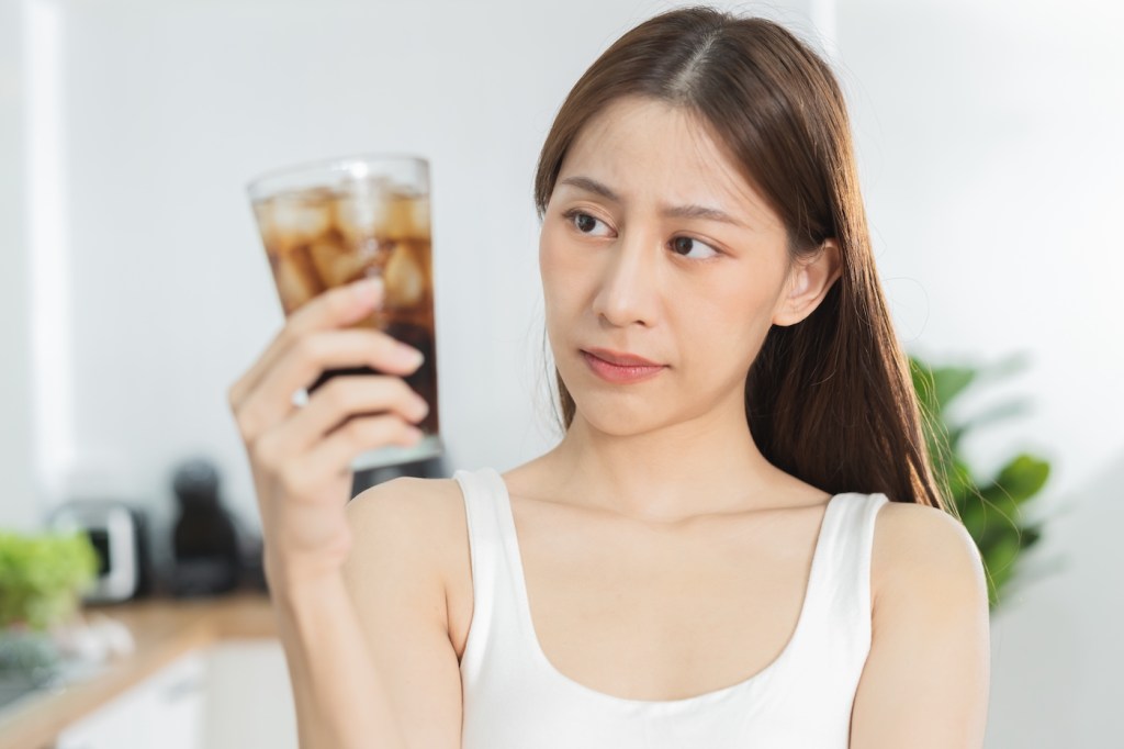 Avoid, limits sweet sugar, choose asian young woman, girl holding, looking at a glass of cold cola soft drink soda, sparkling water with ice by her hand. Health care, healthy diet lifestyle concept.