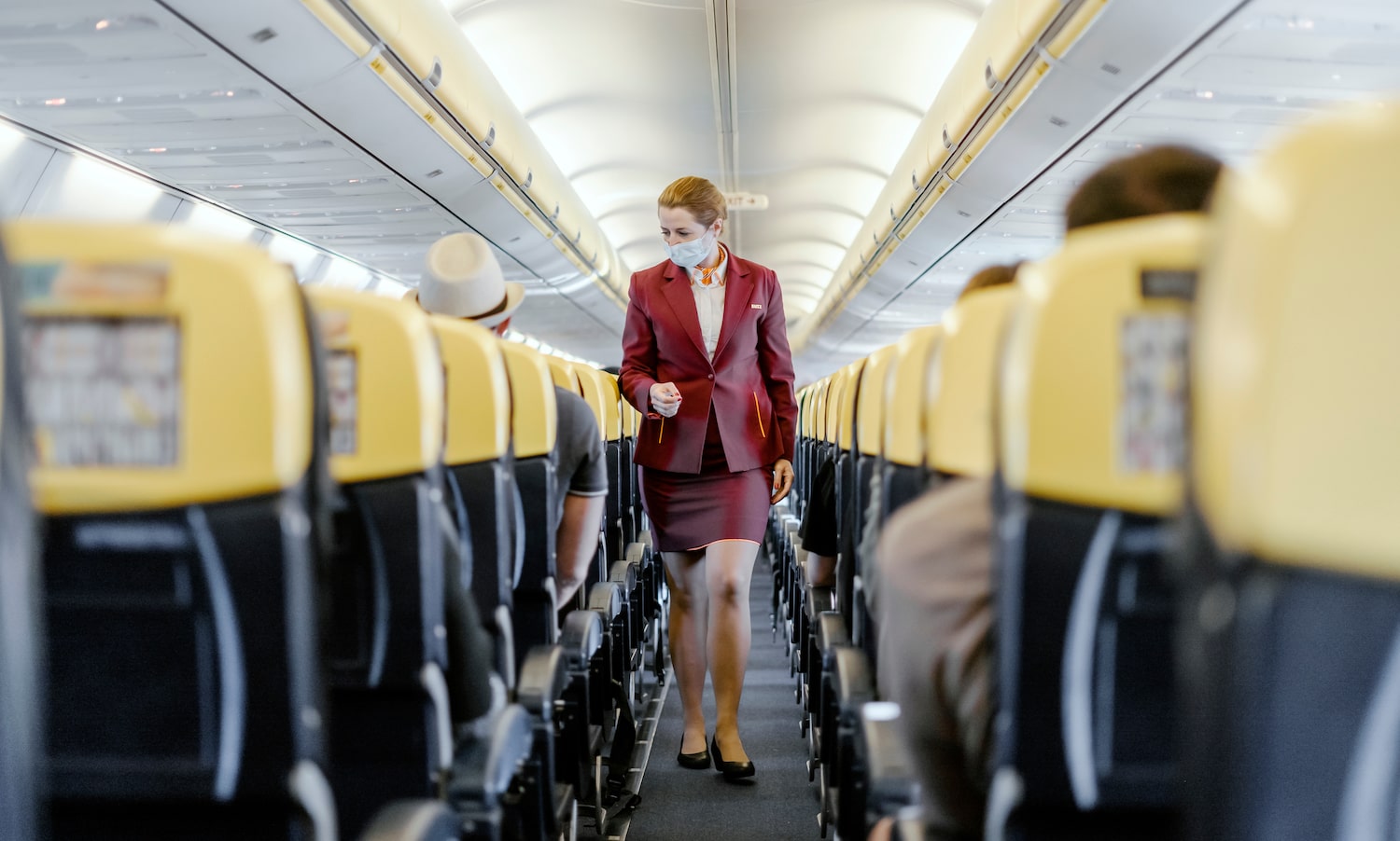 a flight attendant wearing a mask walks through a plane aisle