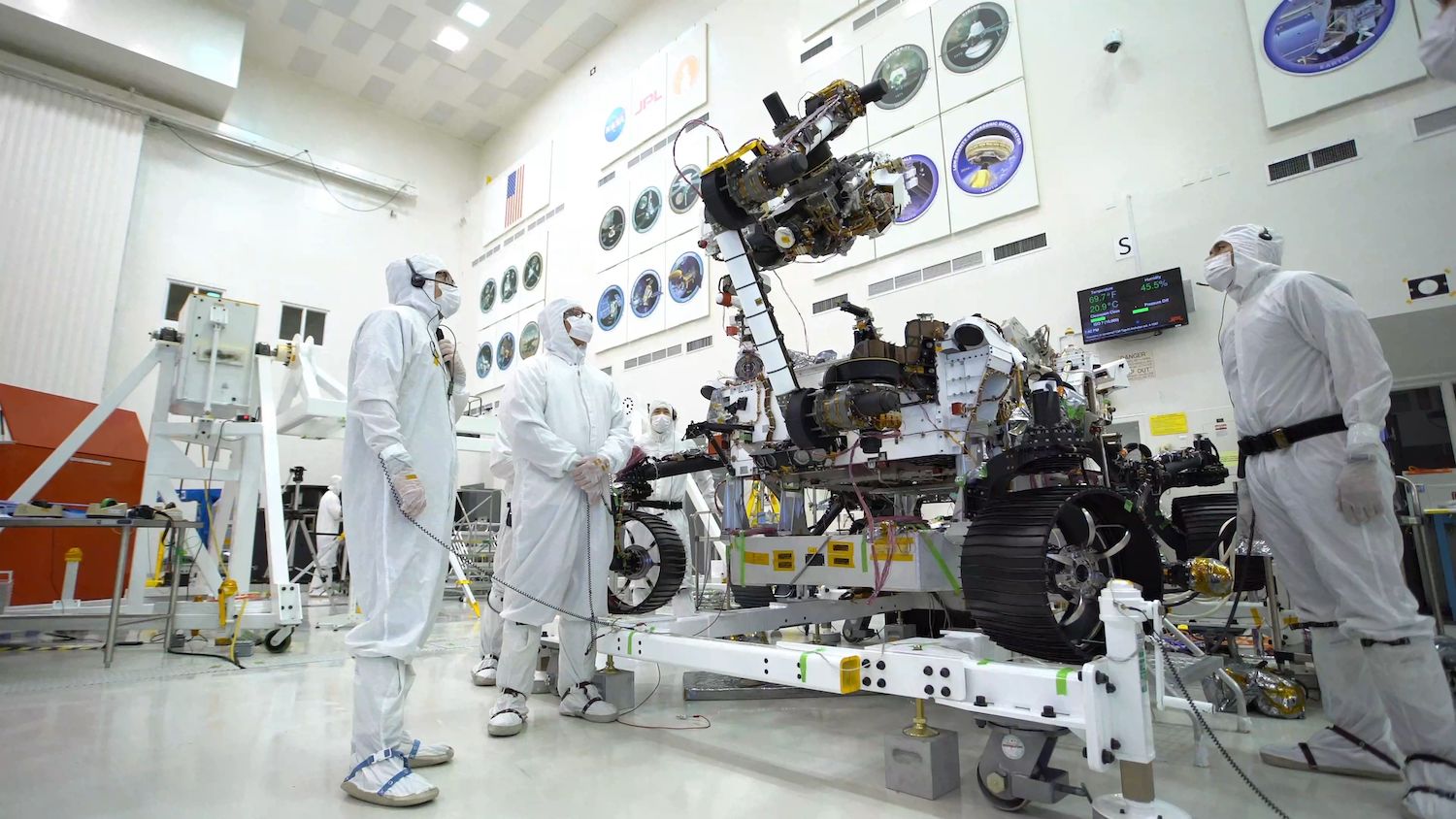 nasa scientists in white sanitation gowns and masks assess and test a mars rover in a lab
