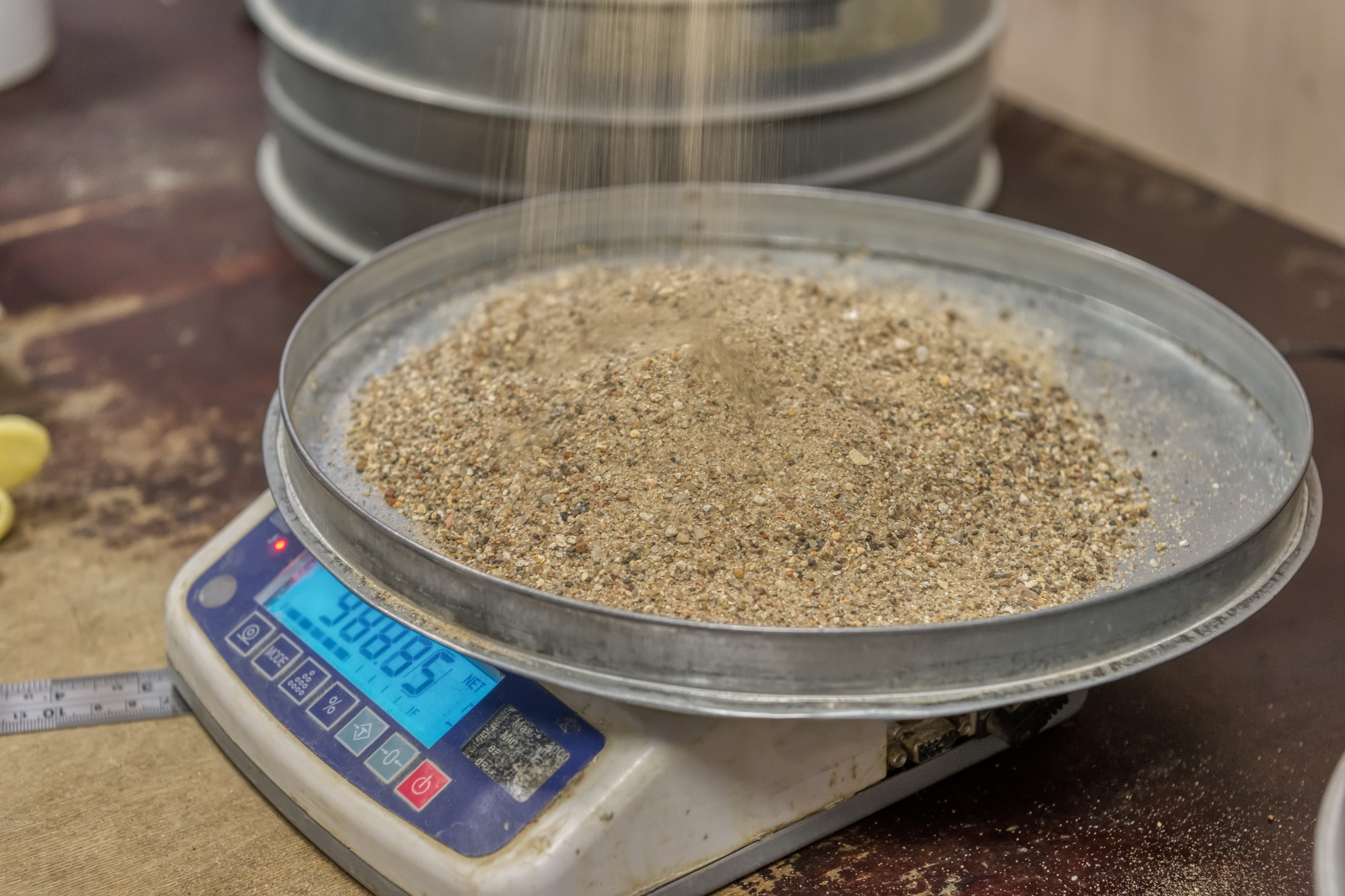 Gritty, tan sand being poured onto a digital scale.