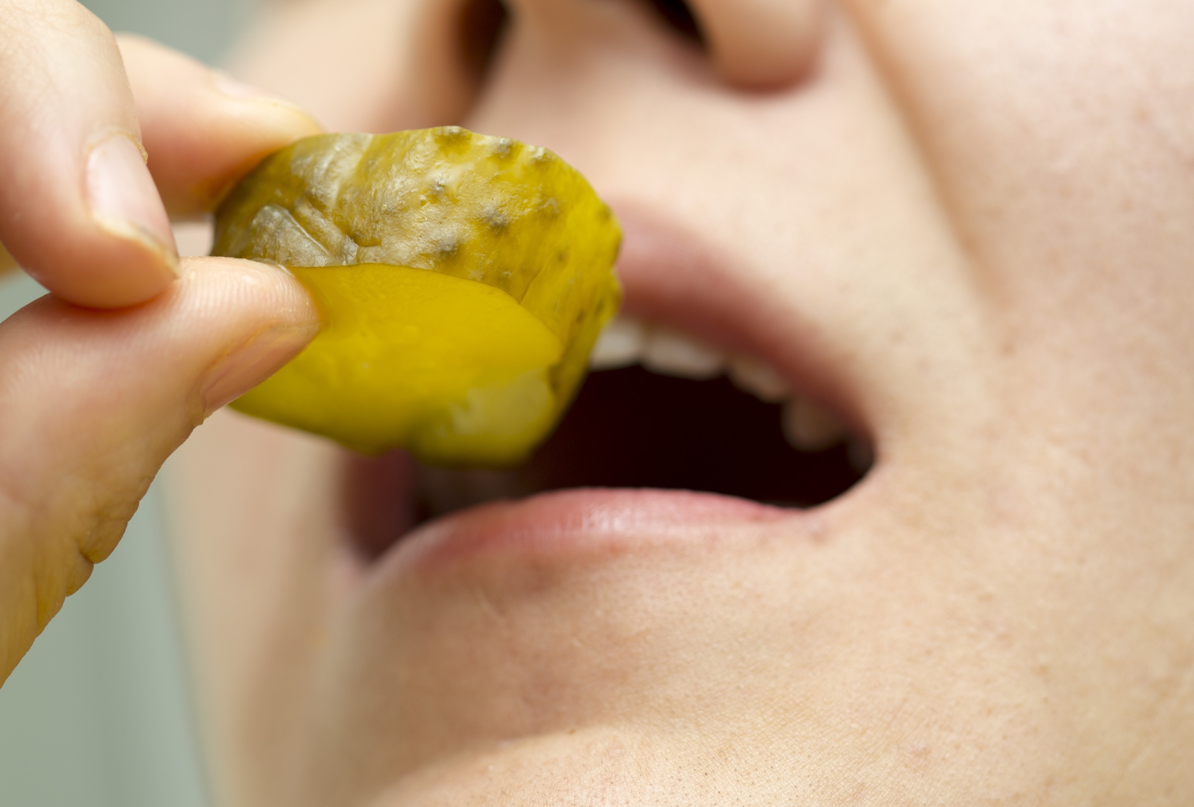 A close-up view of a man eating a bright green-yellow pickle slice.