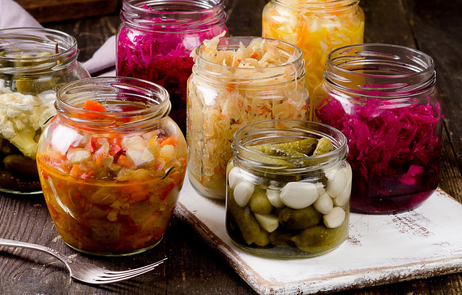 Open glass jars featuring fermented vegetables suck as pickles, kimchee, and sauerkraut.