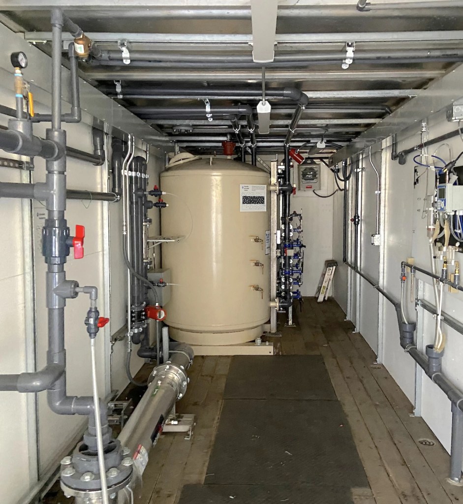 A large metal drum inside a room full of pipes.