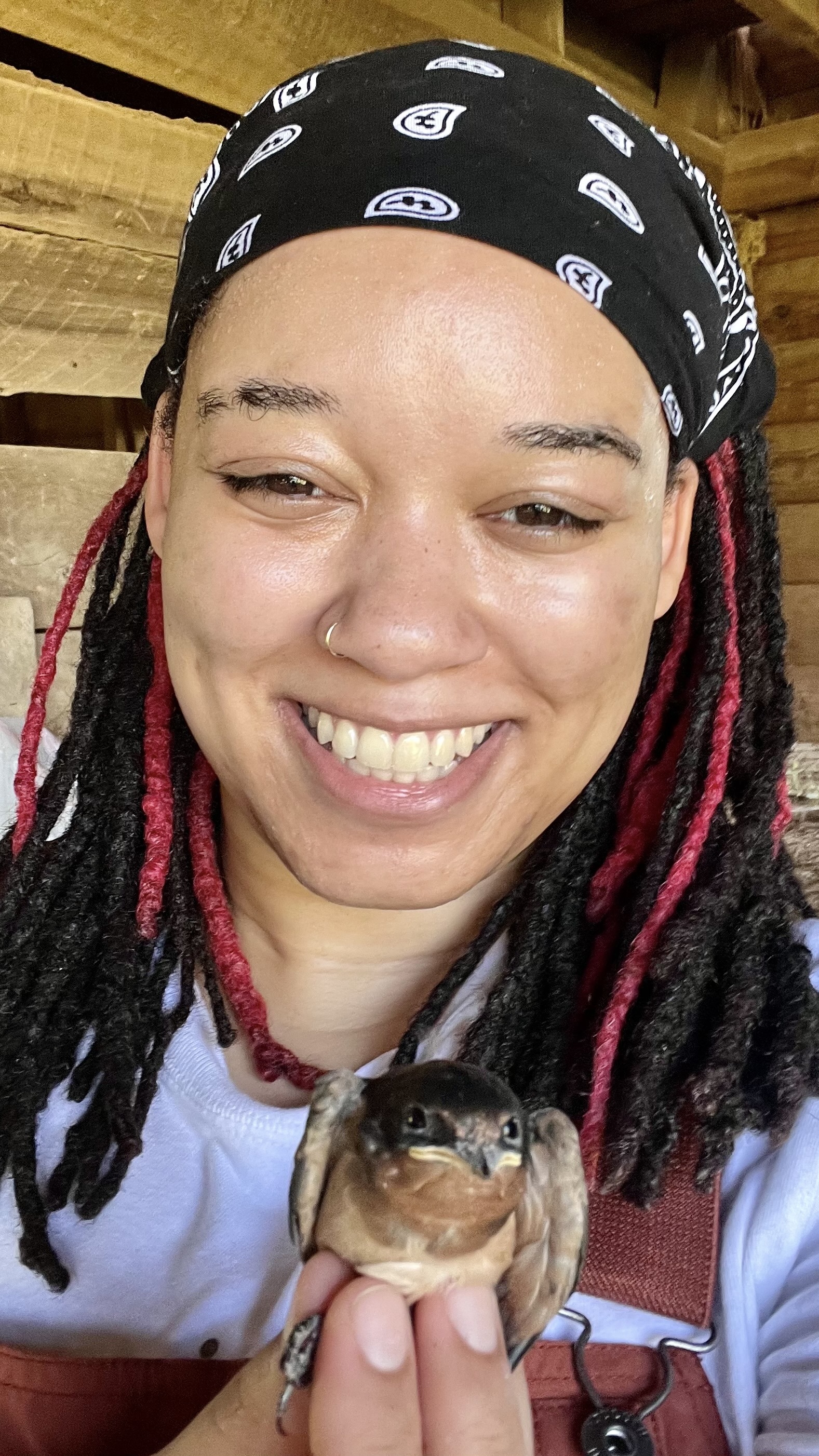 A smiling woman wearing a bandana holds a bird in her hand