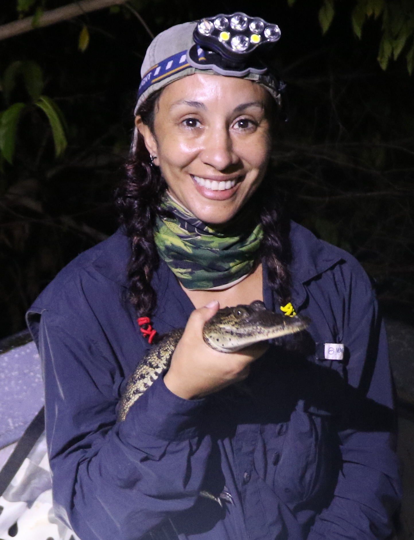 A woman holding a tiny crocodile with a headlamp on.