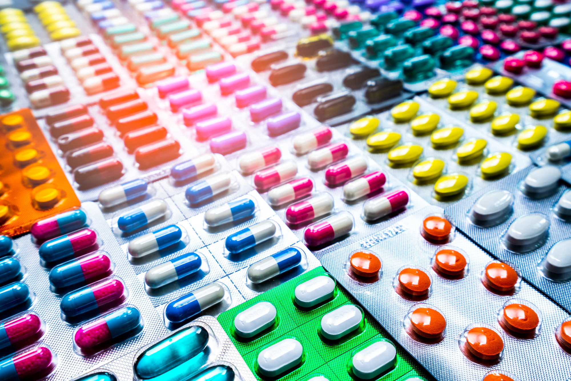 Rows of blister packs containing colorful pills and tablets fill the frame.