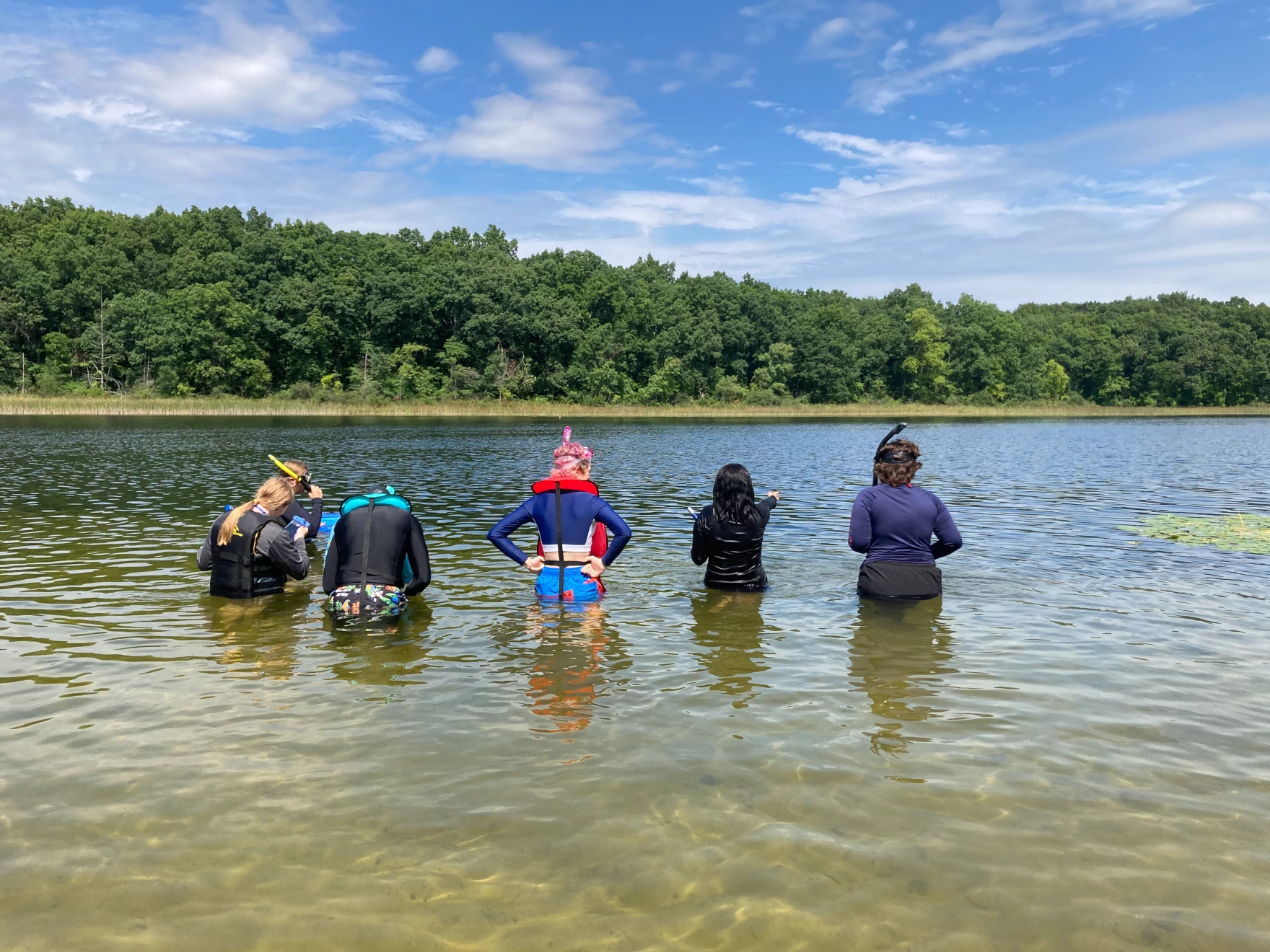 5 people standing in waist high water, looking down into it.